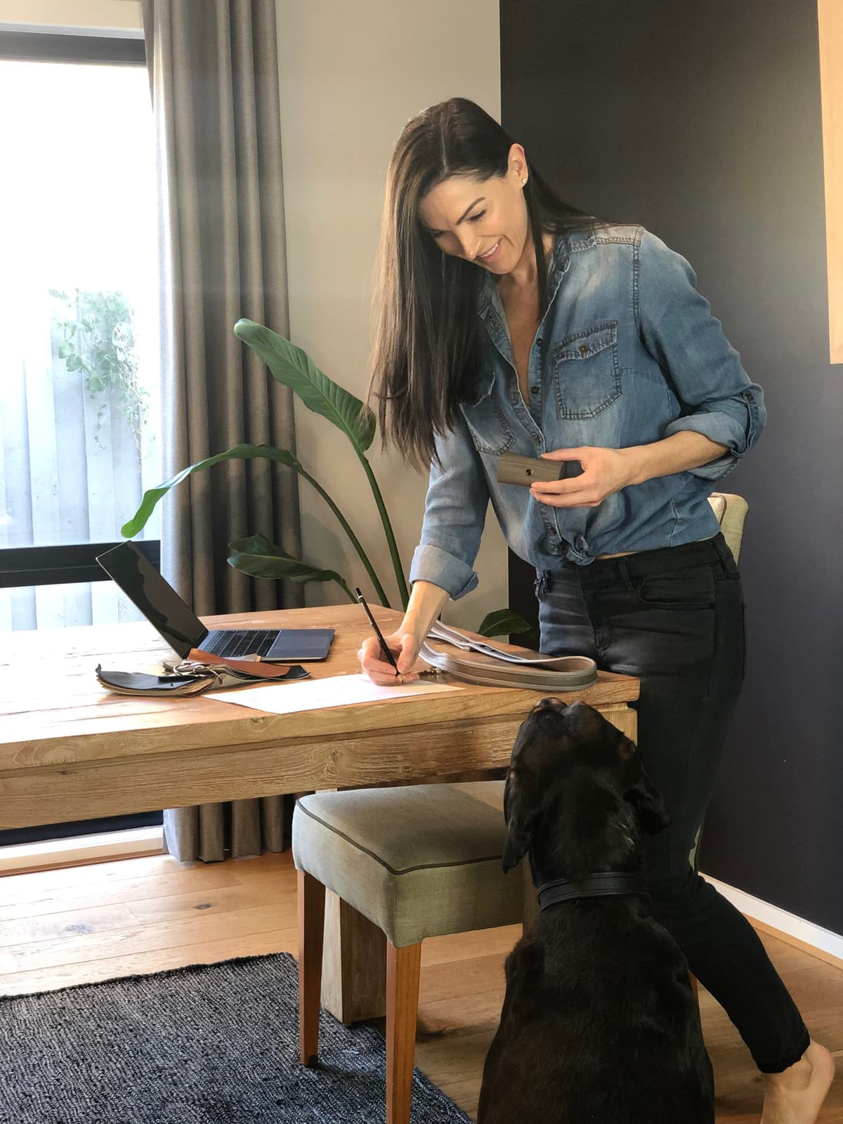 Molly Barker designing luxury pet accessories at her desk with leather samples and her black dog.