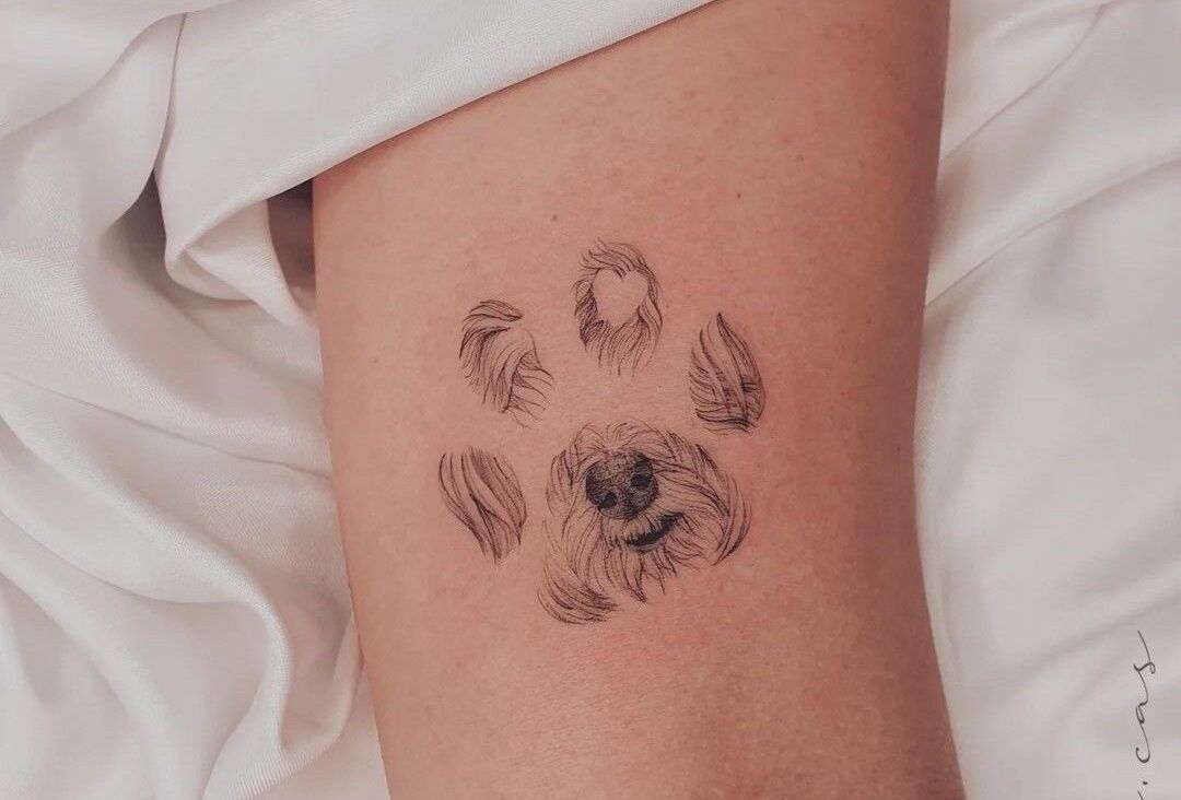 A fine-line tattoo on skin of a dog's snout and fur arranged into the shape of a paw print.
