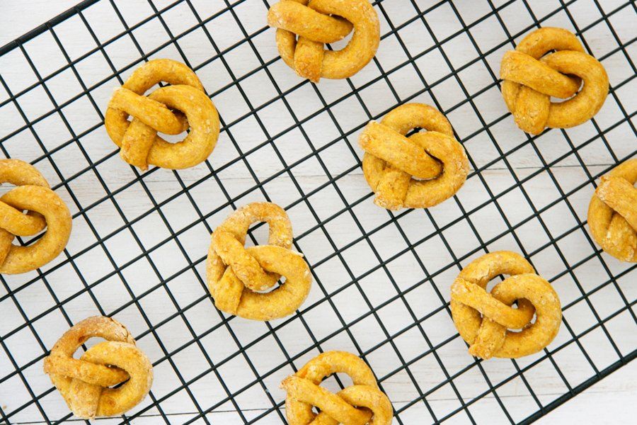 Homemade sweet potato pretzel dog treats cooling on a black wire rack.