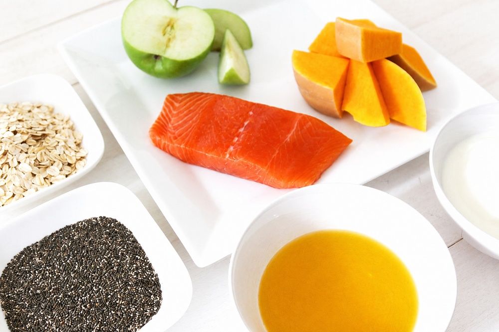 Raw salmon, green apple, squash, oats, chia seeds, broth, and yogurt arranged in white dishes.