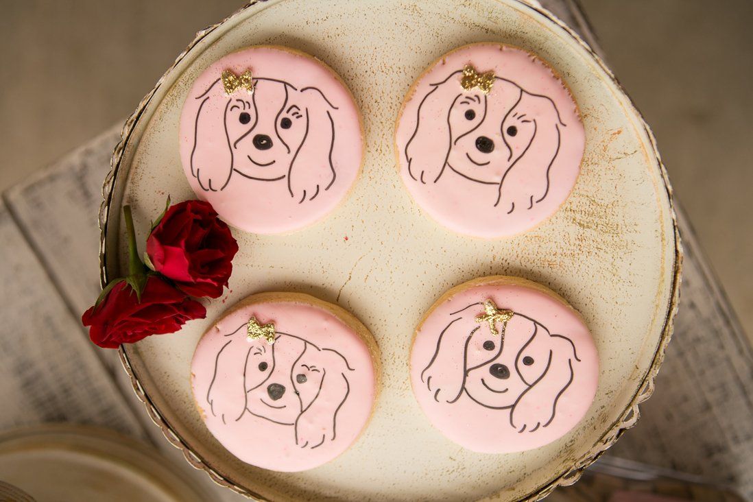 Pink sugar cookies with spaniel dog illustrations and gold bows on a platter for a dog lovers meetup party.