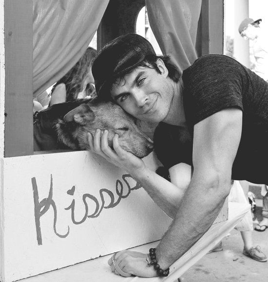 Black and white lifestyle photography of Ian Somerhalder cuddling a dog at a kissing booth.