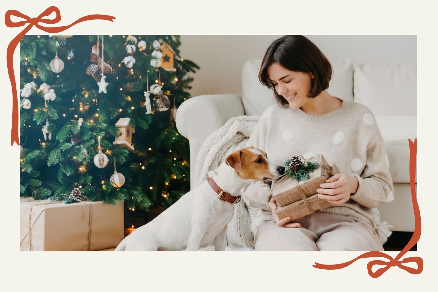 Woman holding Christmas gifts next to her Jack Russell Terrier by a decorated tree; holiday ideas for dog lovers.