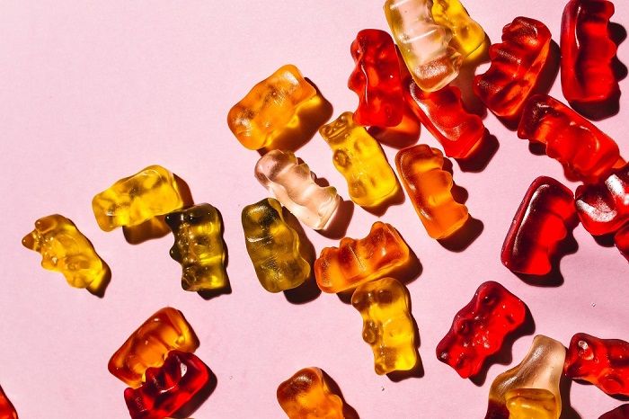Colourful gummy bear candies scattered on a pink background.