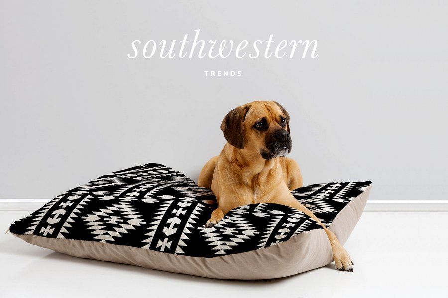 A tan dog lounging on a stylish black and white Southwestern pattern dog bed.