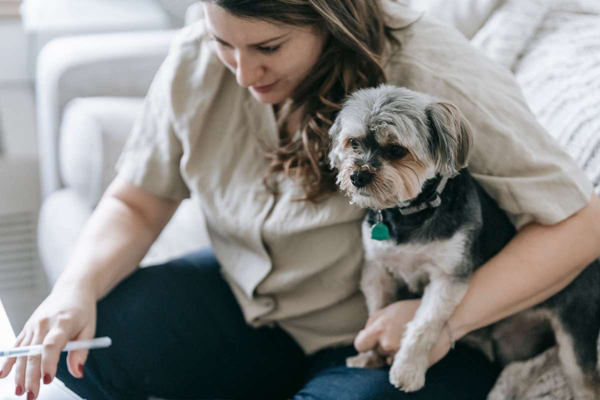 A woman holds a small scruffy dog on her lap while holding a pen.
