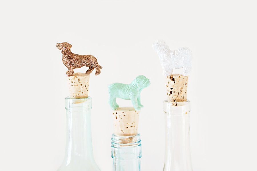 Three DIY dog wine stoppers made with painted dog figurines and corks in glass bottles.
