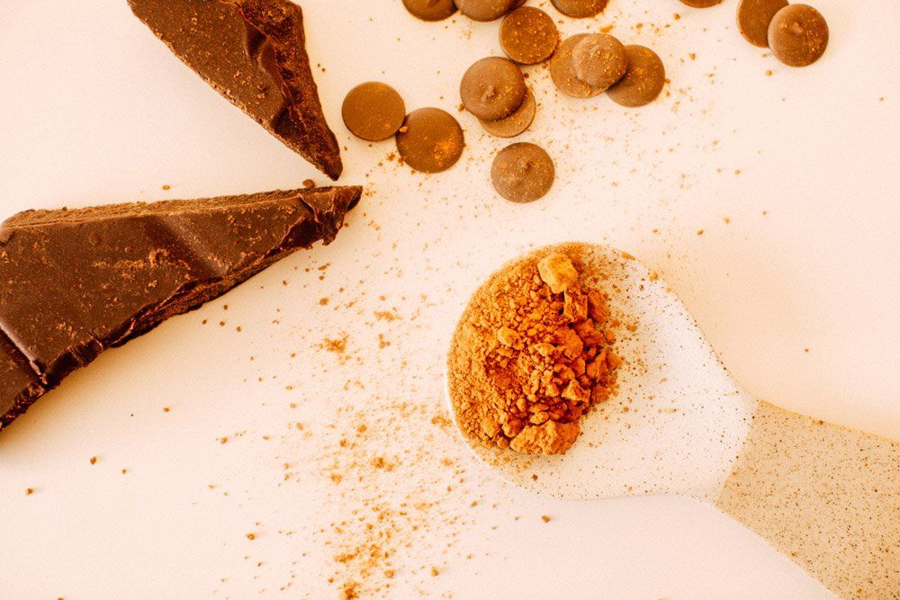 Carob powder on a spoon with carob chips and chunks, a chocolate alternative for safe and healthy dog treats.