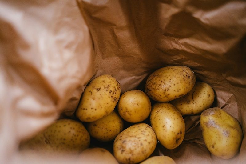 Unwashed potatoes clustered inside a crumpled brown paper bag.