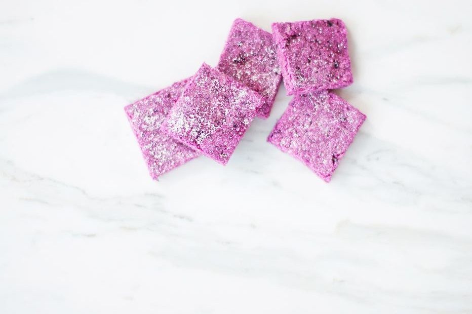 Square-cut pink banana and beetroot dog treats on a white marble surface from a DIY dog treat recipe.