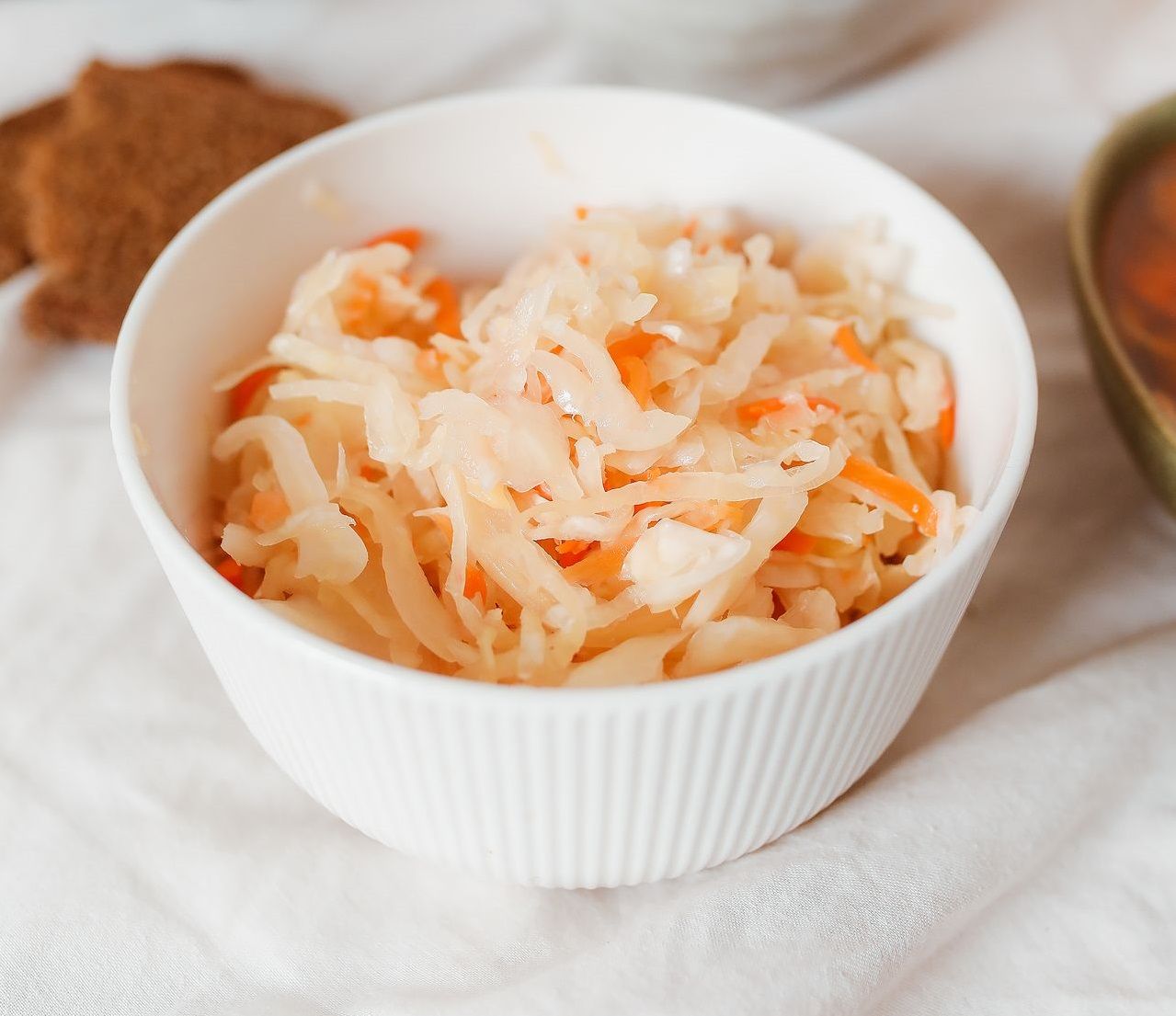 A white bowl of sauerkraut mixed with shredded carrots sits on a table.