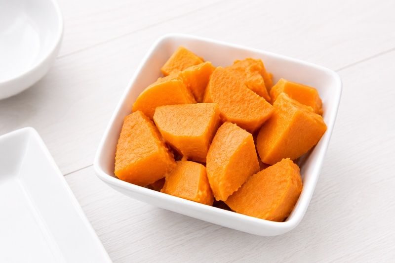 Cooked sweet potato chunks in a square white bowl on a white wooden table.
