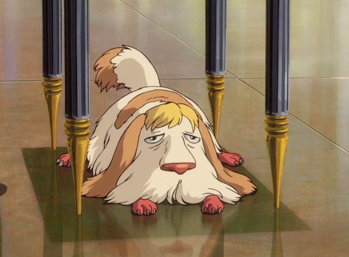 Animated shaggy dog Heen from Howl's Moving Castle lies flat on the floor under a chair.