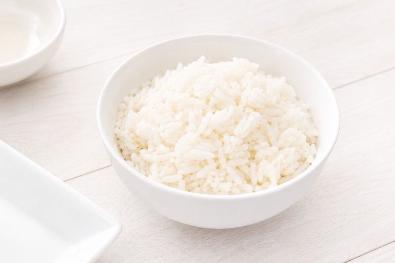 A white bowl filled with plain cooked white rice on a light wooden table.
