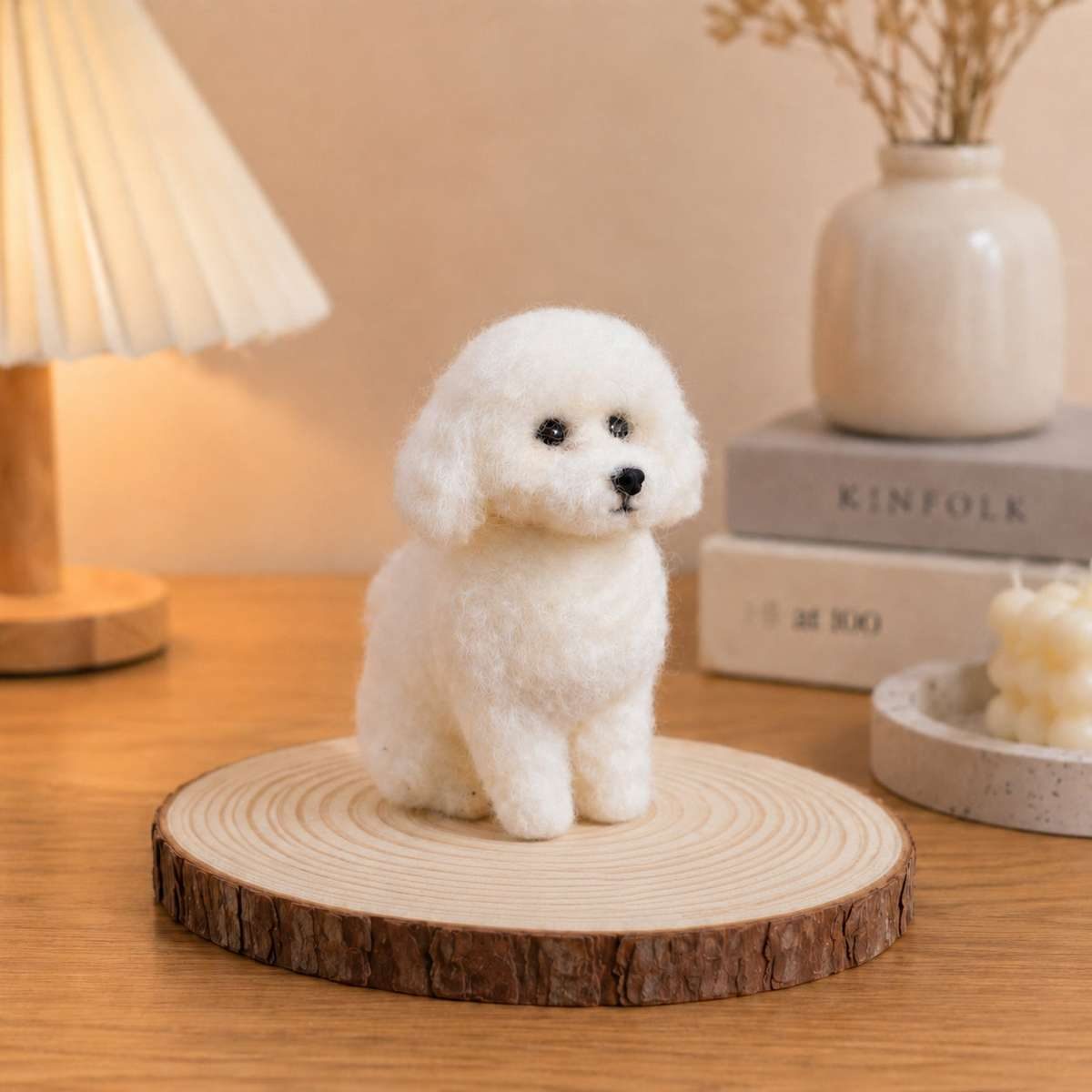 A miniature white needle-felted dog figurine sitting on a round wooden slice.