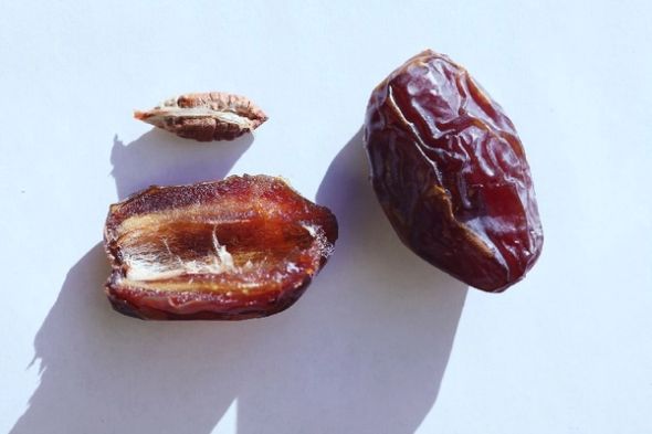 Whole and halved dates with a removed pit on a light background.