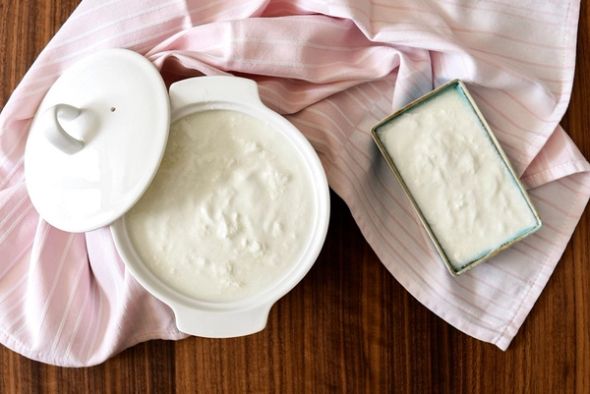 Plain yogurt in white ceramic dishes on a pink striped cloth over a wooden table.