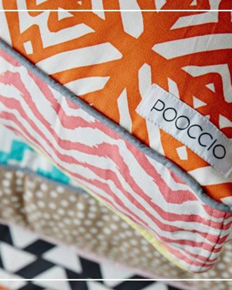 Stacked colorful, patterned dog cushions featuring the POOCCIO luxury dog brand label.