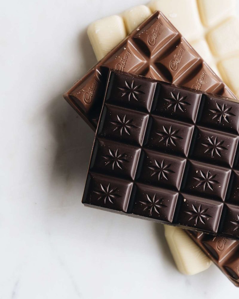 Dark, milk, and white chocolate bars stacked on a light marble surface.