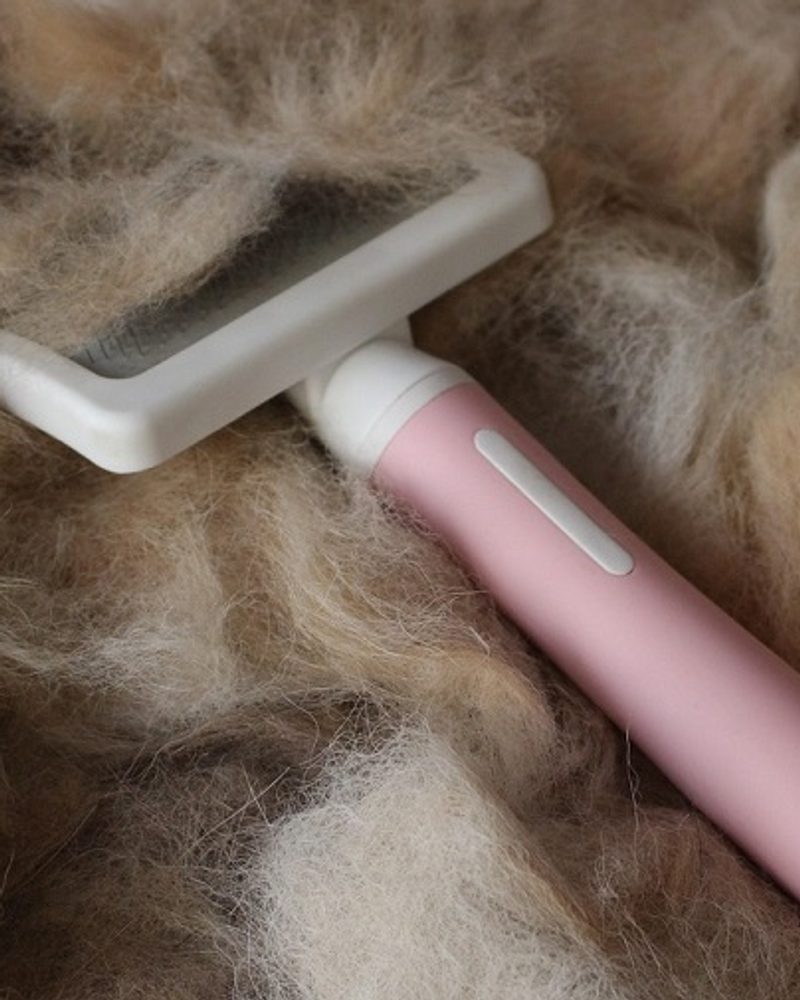 A pink and white pet grooming brush sits on a large pile of shed dog hair.
