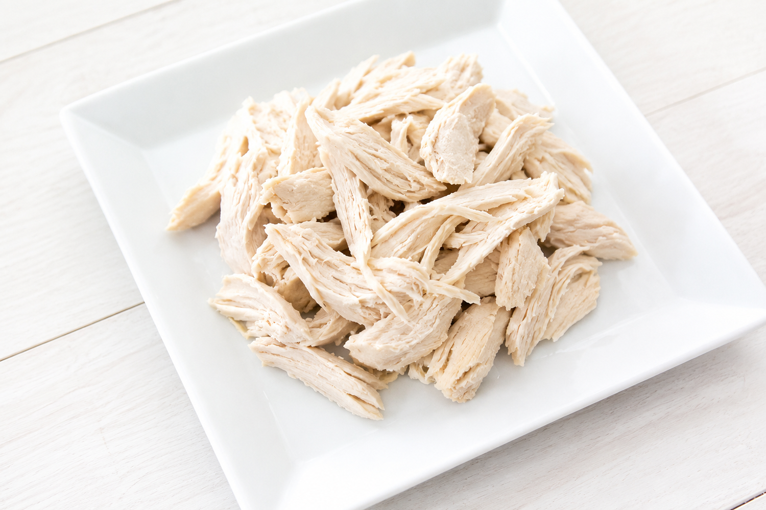 Shredded cooked chicken breast on a square white plate.