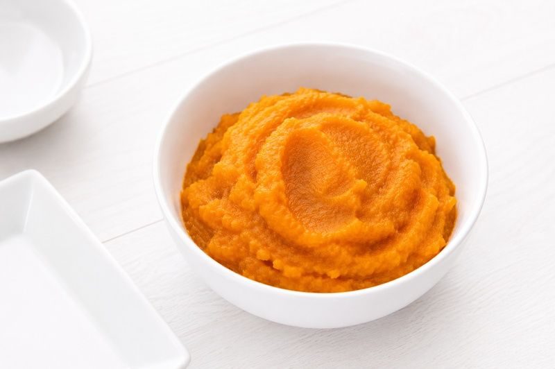 A white bowl filled with smooth orange pumpkin puree on a light wooden surface.
