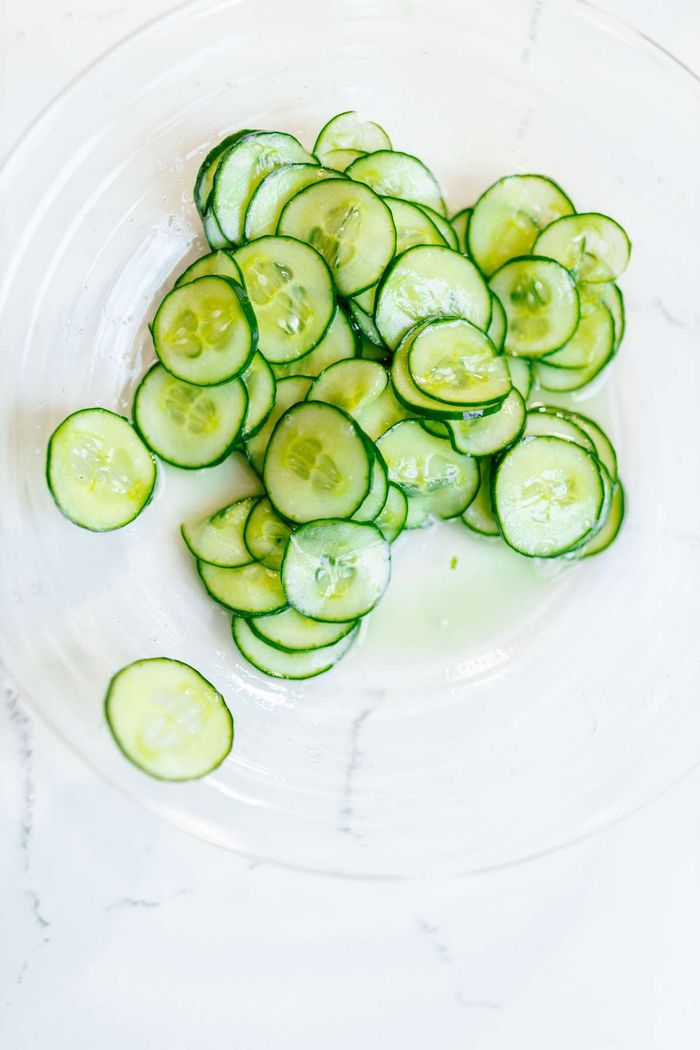Thinly sliced fresh cucumbers in a clear glass bowl on a white countertop.