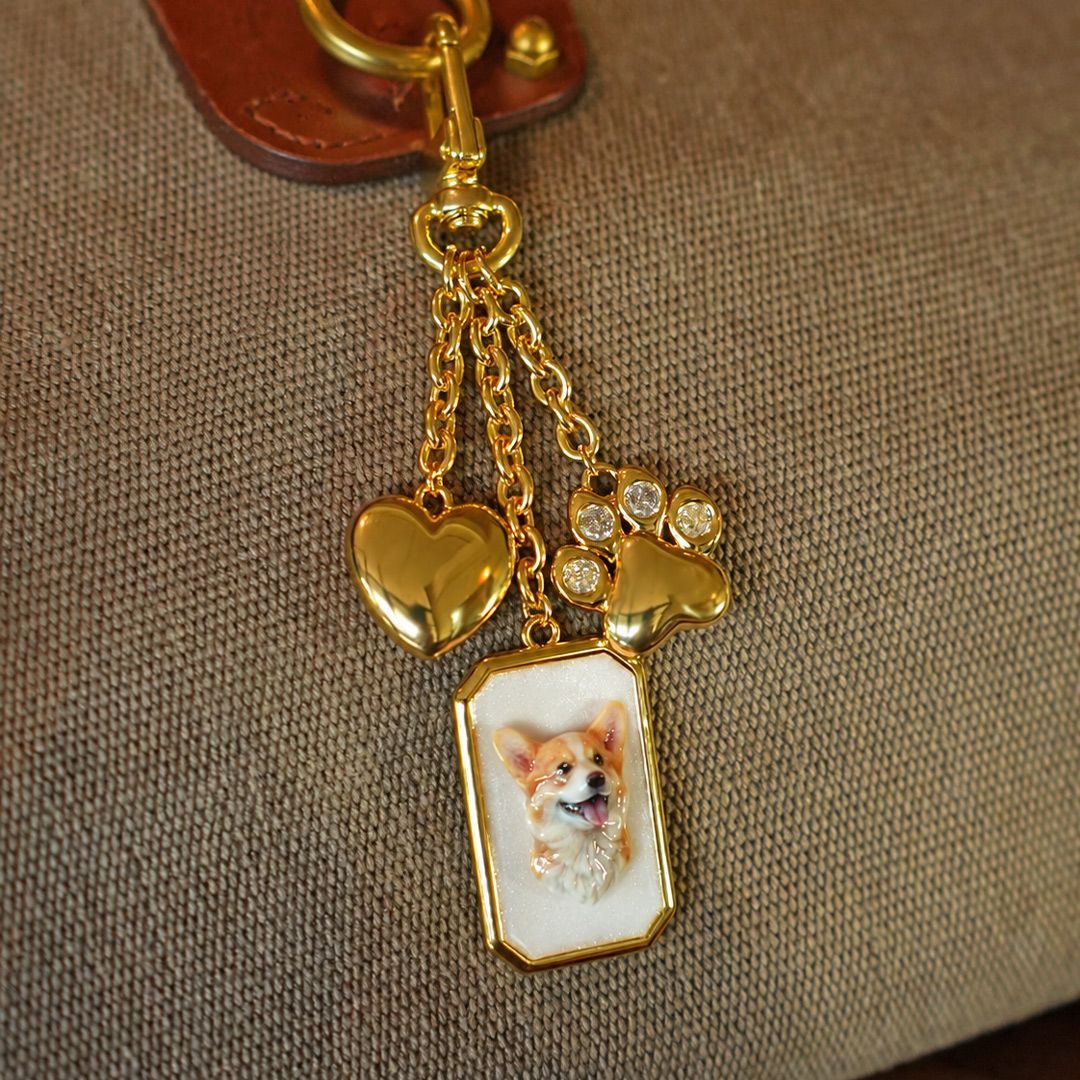A gold bag charm featuring a 3D Corgi portrait, a heart, and a jeweled paw print on a canvas bag.
