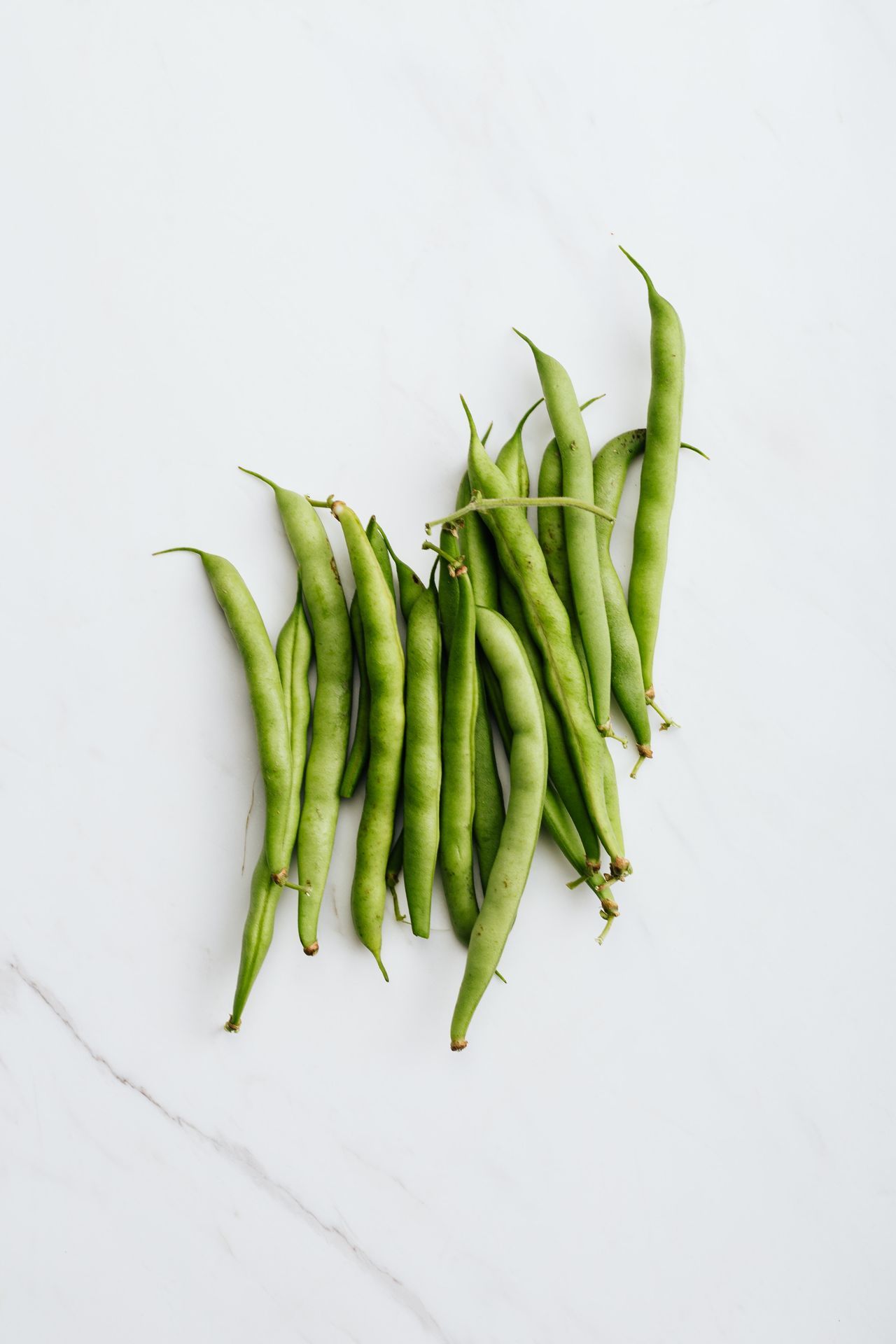 A pile of fresh green beans on a white marble surface.