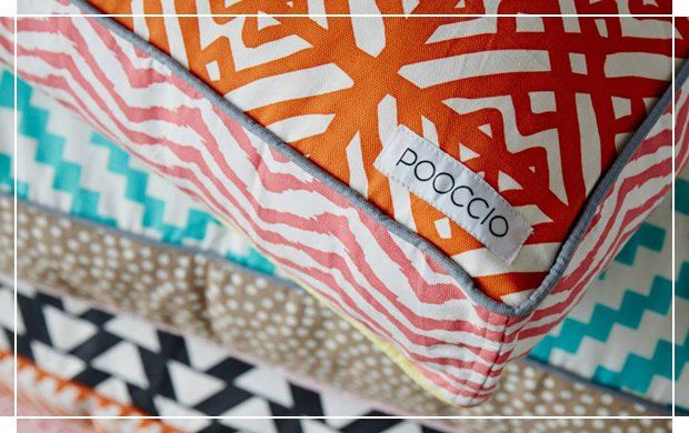 Stacked colorful, patterned dog cushions featuring the POOCCIO luxury dog brand label.