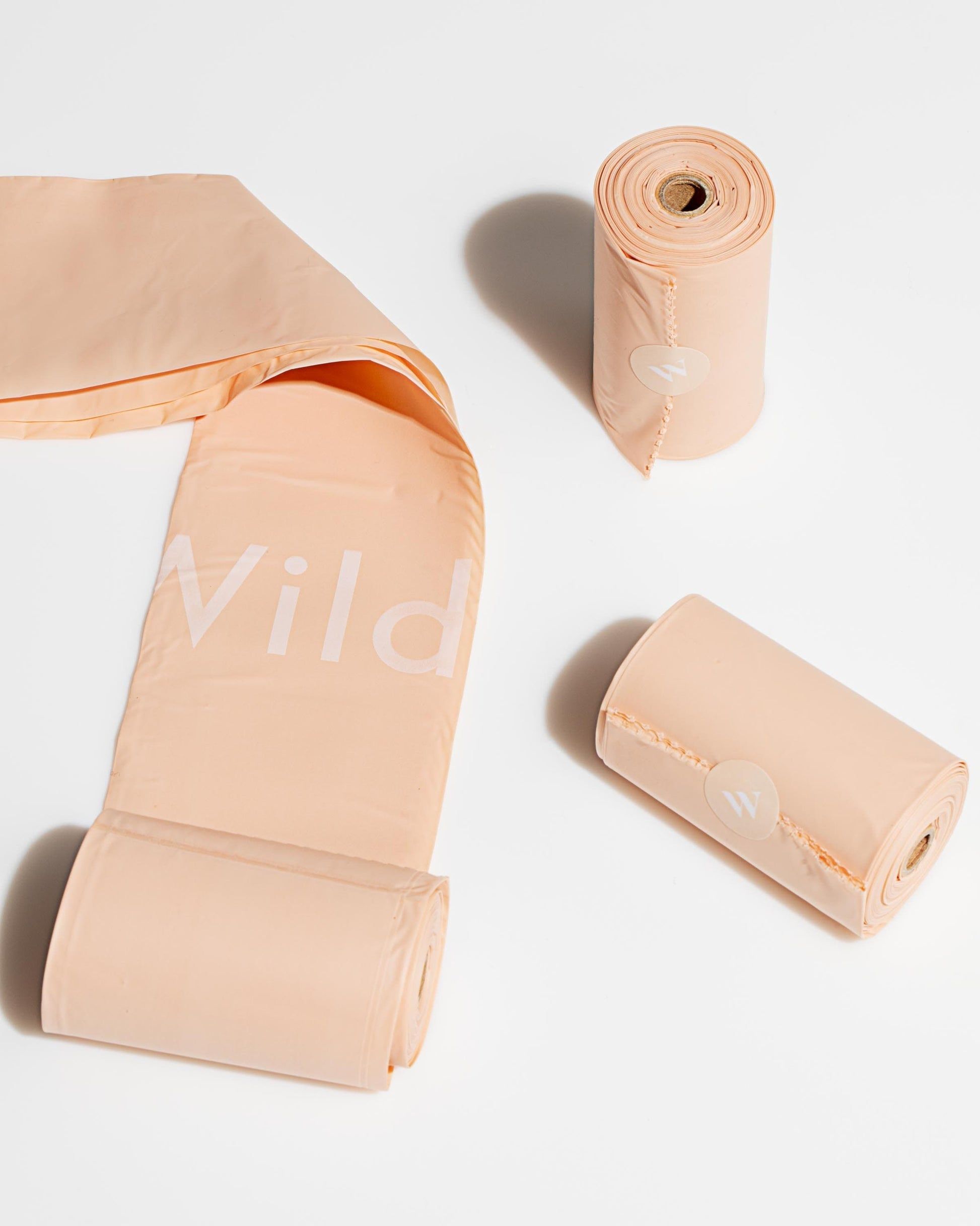 Three rolls of peach-colored dog waste bags on a white background, with one partially unrolled.