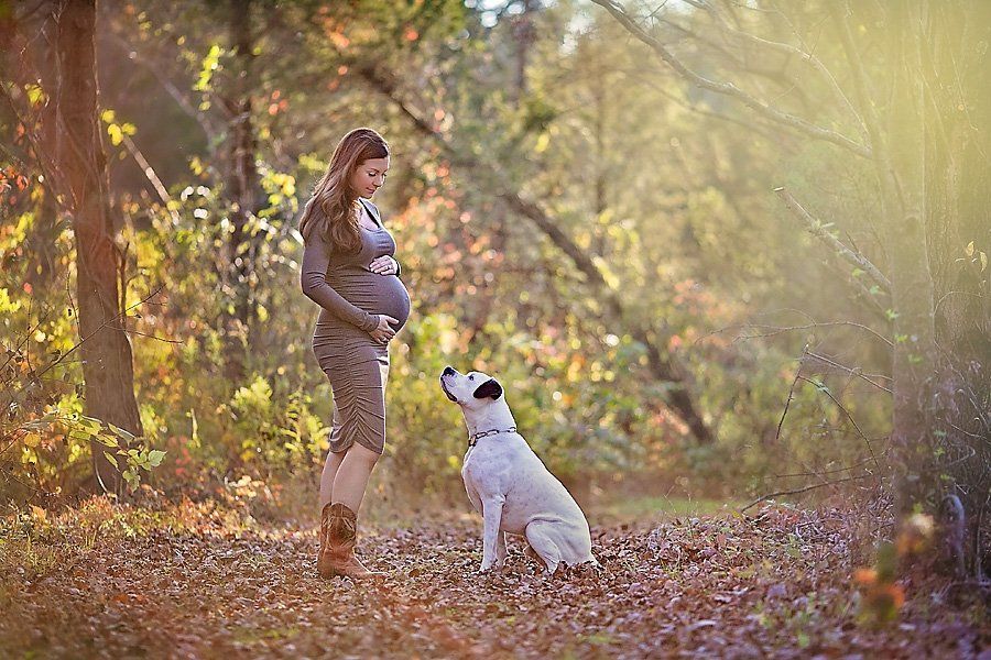 Pregnant woman and white dog in a wooded area for a dog-friendly maternity session by April Ziegler Photography.