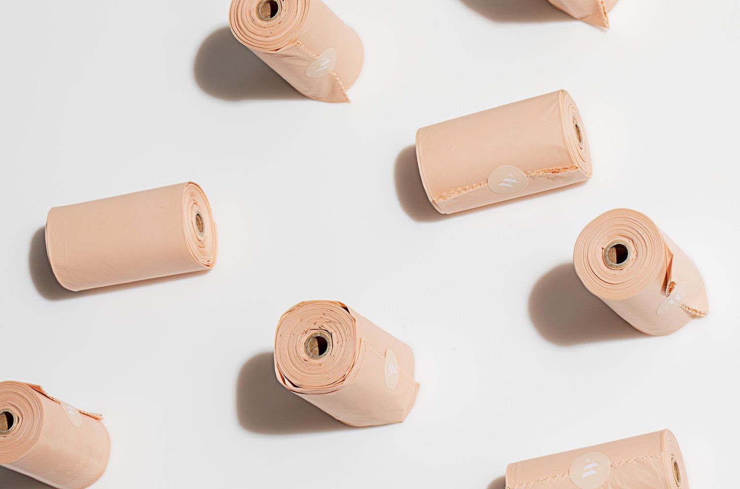 Several rolls of peach dog poop bags scattered across a white surface.
