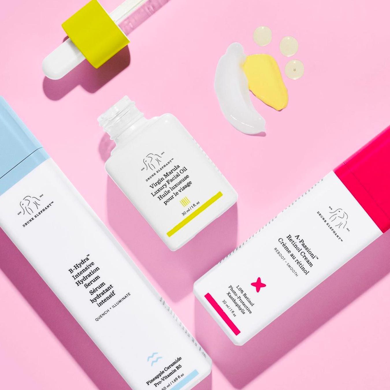 Cruelty-free Drunk Elephant beauty products including B-Hydra serum and Marula oil on a bright pink background.