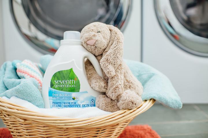 A bottle of Seventh Generation laundry detergent sits in a basket with towels and a plush bunny.