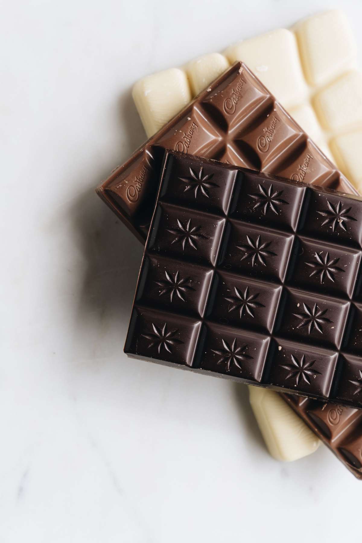 Dark, milk, and white chocolate bars stacked on a light marble surface.
