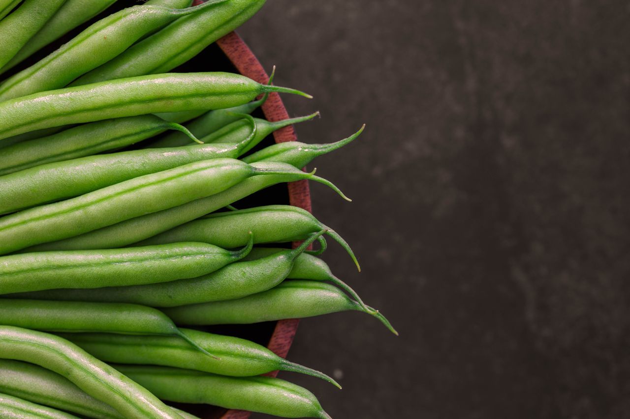 Fresh green beans arranged in a wooden bowl on a dark surface.