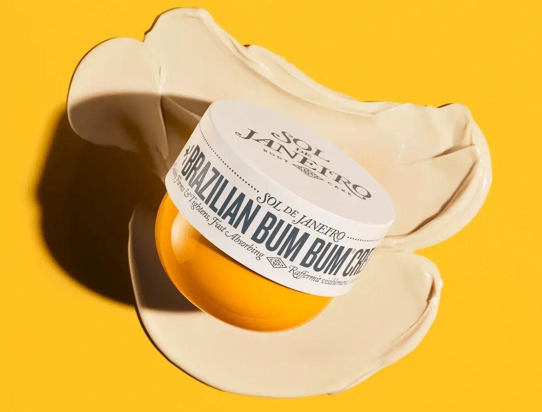 Sol de Janeiro Brazilian Bum Bum Cream jar resting on a swatch of lotion over a bright yellow background.