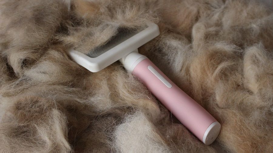 A pink and white pet slicker brush resting on a large pile of shed dog fur.