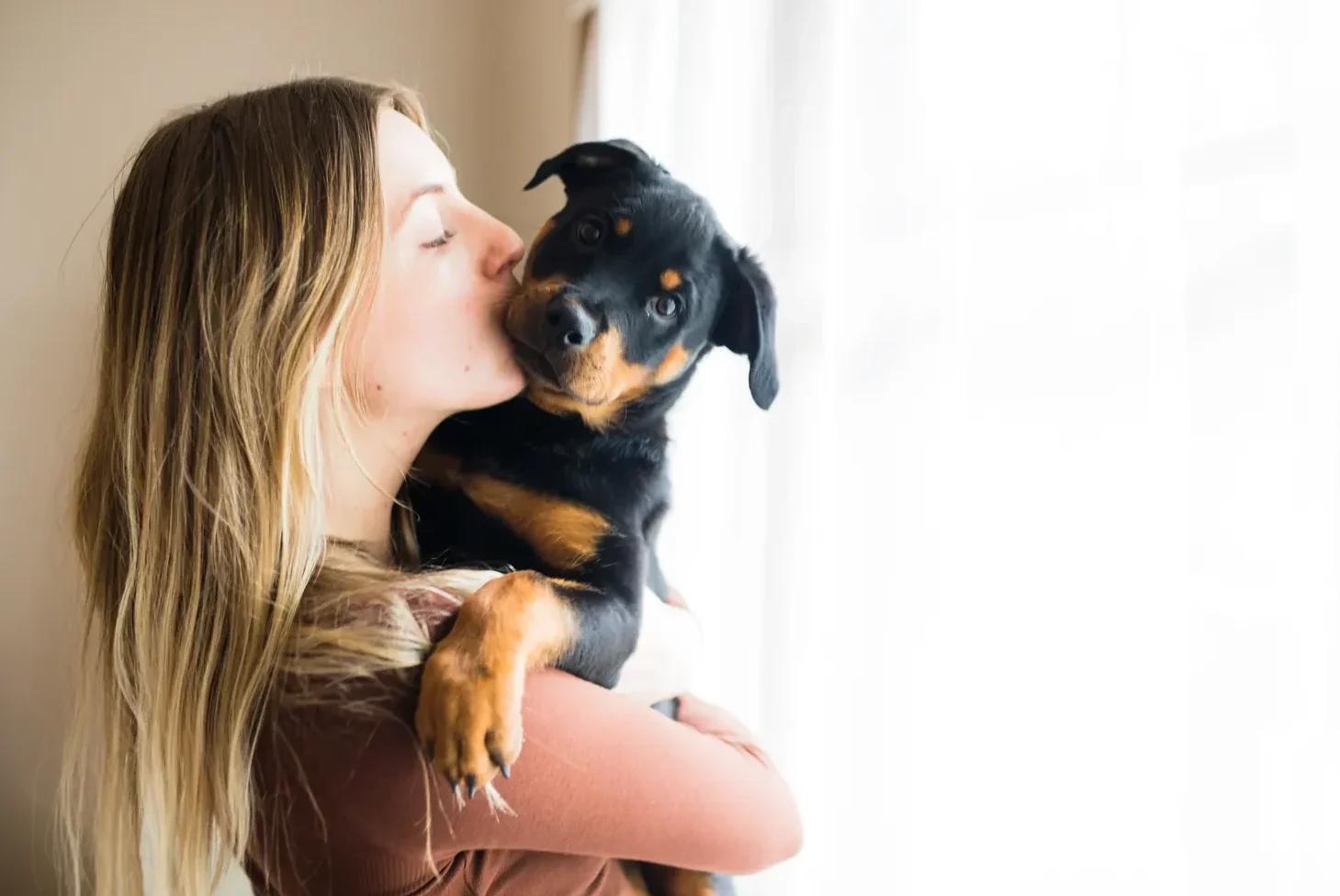 Woman kissing a Rottweiler puppy on the cheek to show how to bond with your puppy through affection.