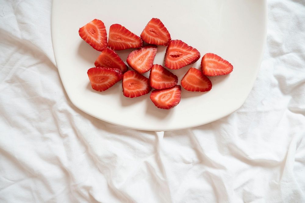 Sliced strawberries arranged on a white plate over a white fabric background.