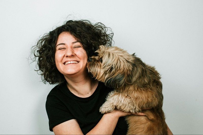 Happy dog mum smiling as her fluffy four-legged mate kisses her cheek.