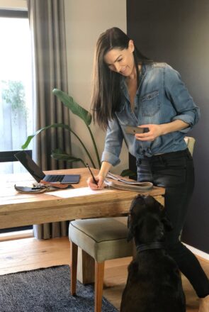 Molly Barker designing luxury pet accessories at her desk with leather samples and her black dog.